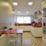 Cozinha planejada com bancada vermelha, armários brancos e iluminação natural no projeto de Aline Zagonel por Marcelo Minuscoli