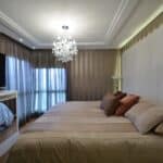 Quarto principal com lustre moderno, cabeceira estofada e cortinas elegantes no projeto de Aline Zagonel por Marcelo Minuscoli